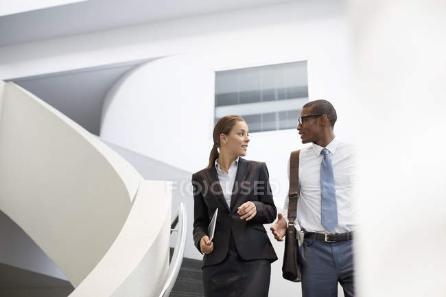 Businessman and businesswoman talking on modern staircase at office — Stock Photo