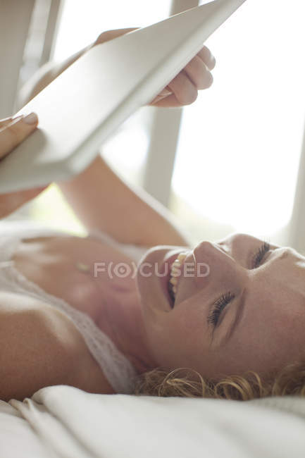Улыбающаяся женщина с помощью цифрового планшета в постели — стоковое фото
