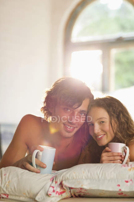 Молодая счастливая пара пьет кофе вместе в постели — стоковое фото