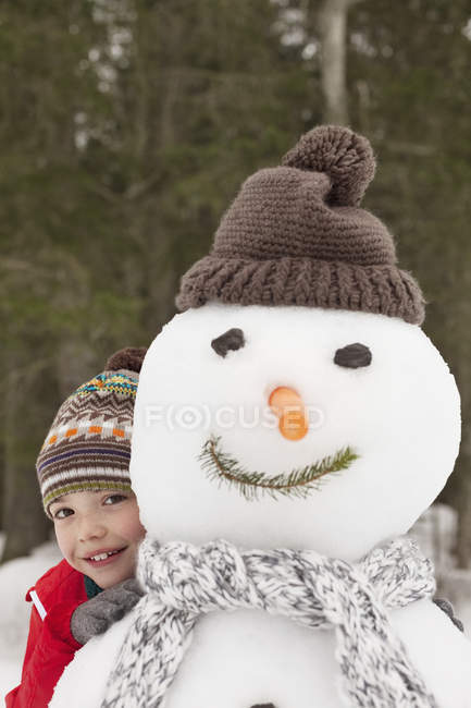 Retrato de niño sonriente detrás de muñeco de nieve con media gorra - foto de stock