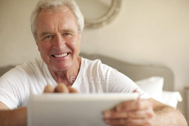 Портрет усміхненого старшого чоловіка, який використовує цифровий планшет у спальні — стокове фото