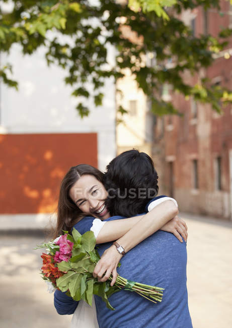 Lächelnde Frau mit Blumen umarmt Mann — Stockfoto