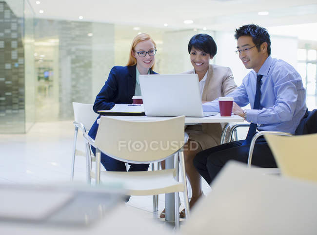 Business people gathered around laptop in office building cafe — Stock Photo