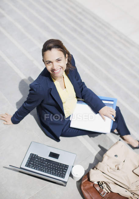 Портрет усміхненої бізнес-леді з паперовою роботою, кавою та ноутбуком на етапах — стокове фото