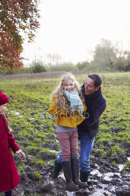 Padre e hija riendo en el campo fangoso - foto de stock