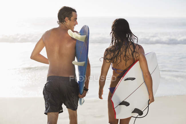 Glückliches kaukasisches Paar spaziert mit Surfbrettern am Strand — Stockfoto