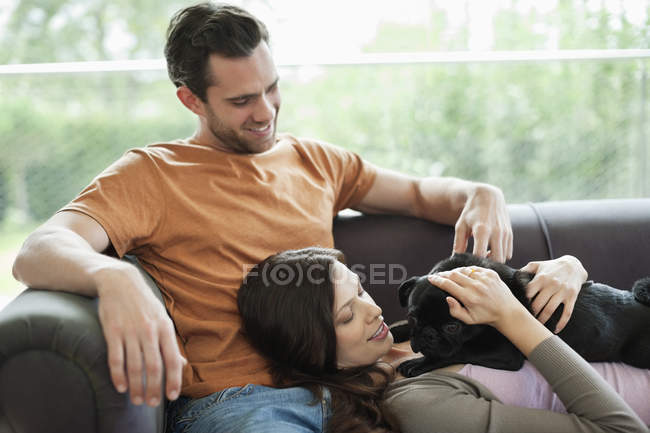 Пара розслабляється з собакою на дивані в сучасному будинку — стокове фото