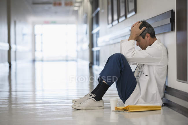Doctor sitting on floor in hospital corridor with head in hands — Stock Photo