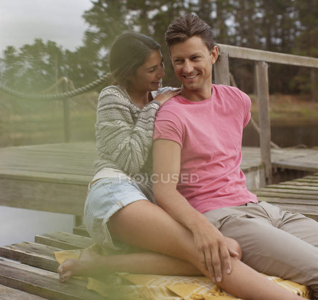 Smiling couple sitting on dock over lake — Stock Photo