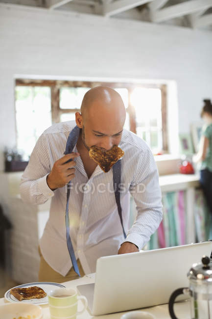 Empresario desayunando y usando laptop - foto de stock