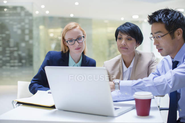 Business people gathered around laptop in office building cafe — Stock Photo