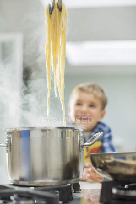 Niño viendo padres cocinar espaguetis - foto de stock