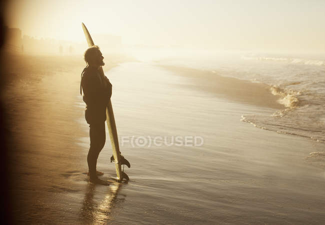 Surfista de pie con tabla en la playa - foto de stock