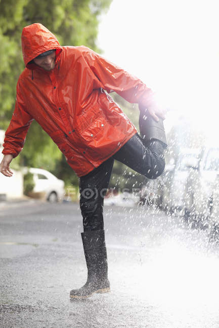 Человек, стоящий на одной ноге на дождливой улице — стоковое фото