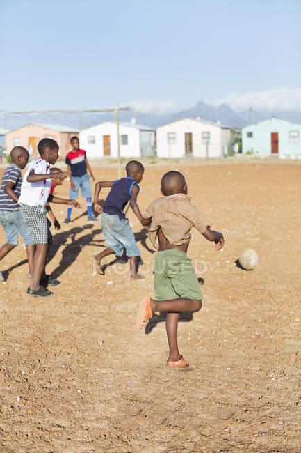 Garçons africains jouant au football ensemble dans un champ de terre — Photo de stock