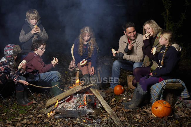 Family eating around campfire at night — Stock Photo