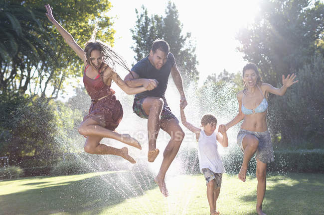Felice famiglia caucasica saltando in irrigatore — Foto stock