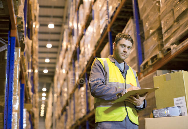 Worker writing on clipboard in warehouse — Stock Photo