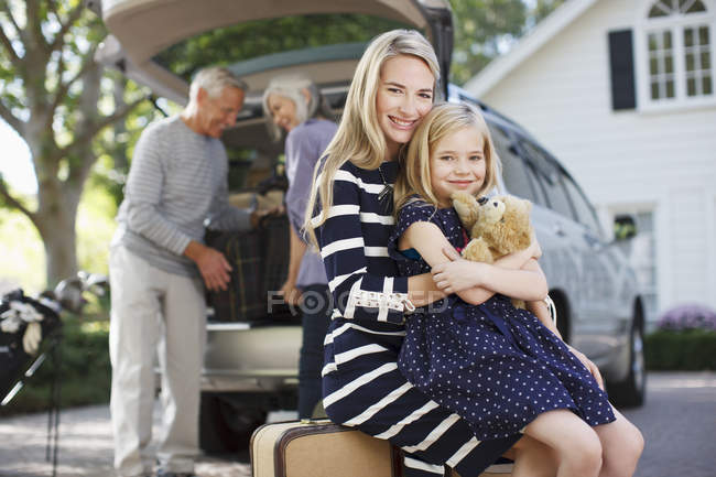 Smiling mother and daughter sitting on luggage — Stock Photo