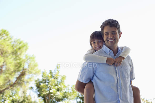 Father carrying daughter piggy back outdoors — Stock Photo