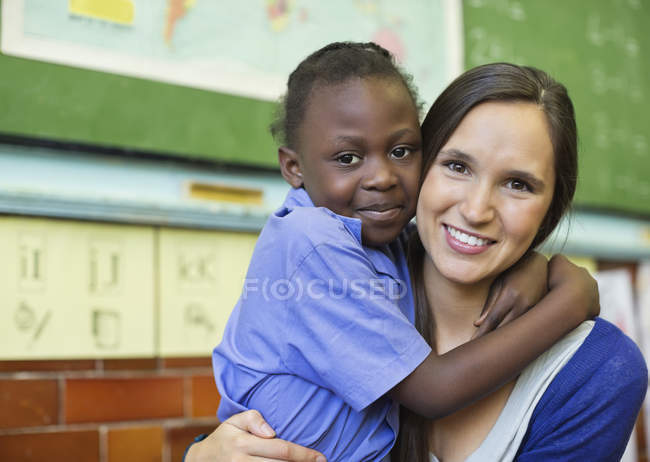 Profesora abrazando a estudiante afroamericano en clase - foto de stock