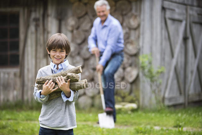 Boy carrying pile of firewood outdoors — Stock Photo