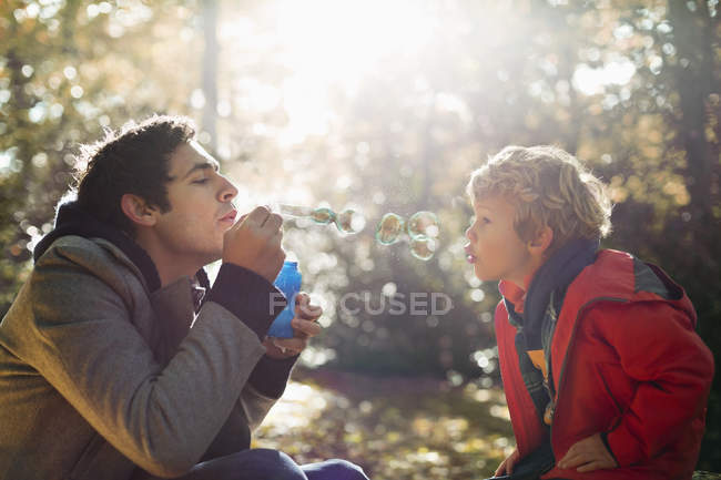 Padre e hijo soplando burbujas en el parque - foto de stock