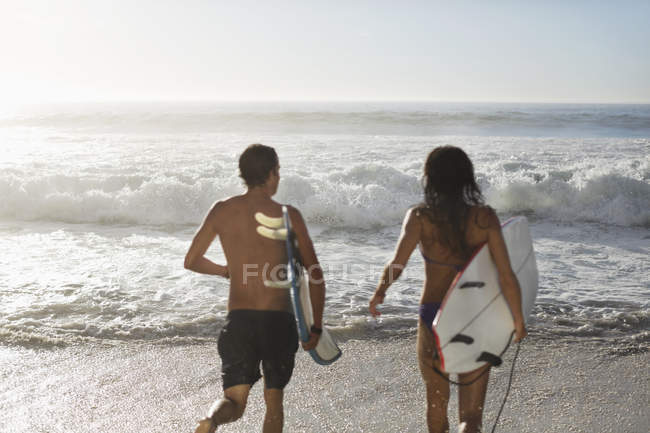 Pareja corriendo con tablas de surf hacia el océano - foto de stock