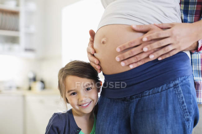 Girl smiling with pregnant mothers belly — Stock Photo