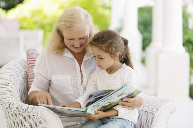 Mujer mayor leyendo a su nieta en el porche - foto de stock