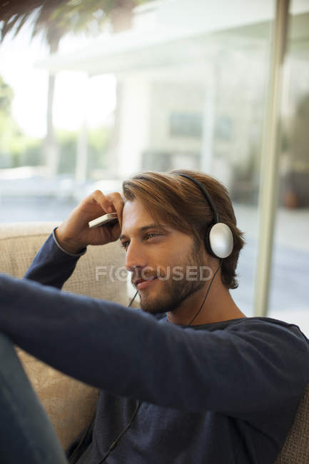 Молодий привабливий чоловік слухає навушники на дивані — стокове фото
