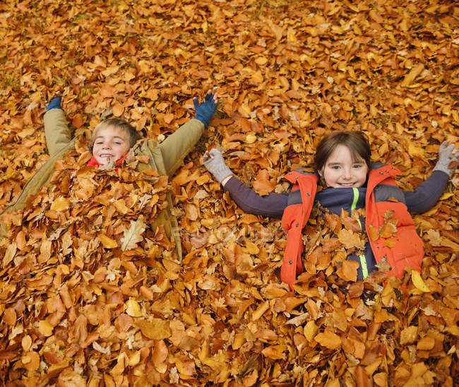 Bambini felici che posano in foglie di autunno — Foto stock