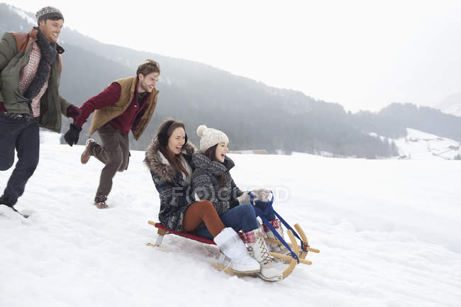 Enthusiastic friends sledding in snowy field — Stock Photo