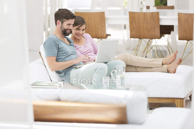 Casal usando laptop juntos na cama de dia na sala de estar moderna — Fotografia de Stock