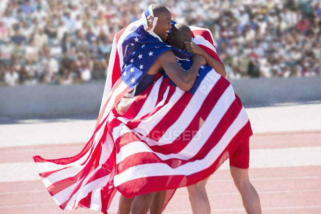 Track and field athletes wrapped in American flag on track — Stock Photo