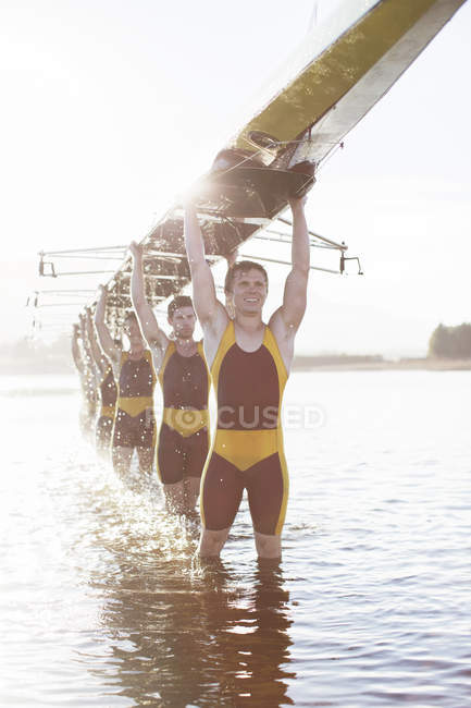 Rowing team carrying scull overhead in lake — Stock Photo