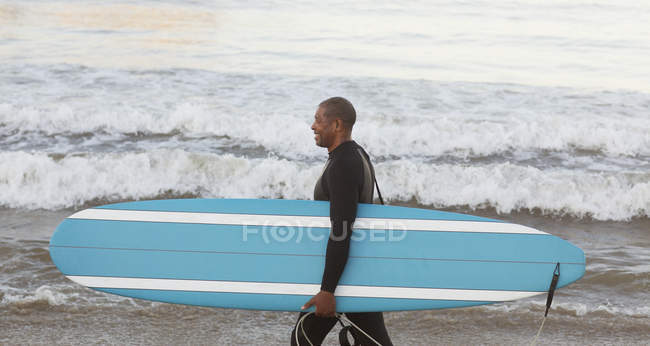 Surfista più anziano che trasporta bordo sulla spiaggia — Foto stock