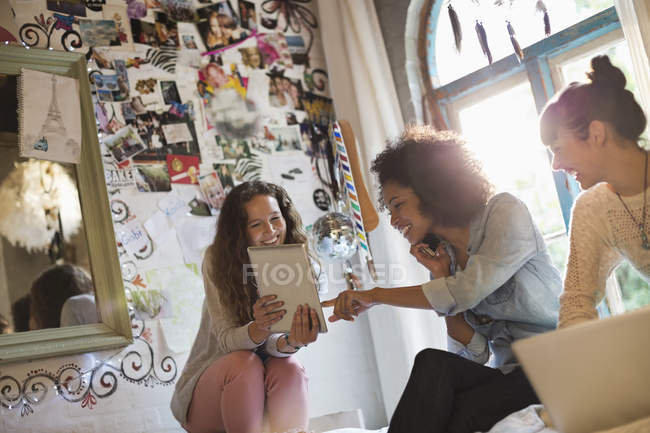 Young happy women relaxing together in bedroom with digital devices — Stock Photo