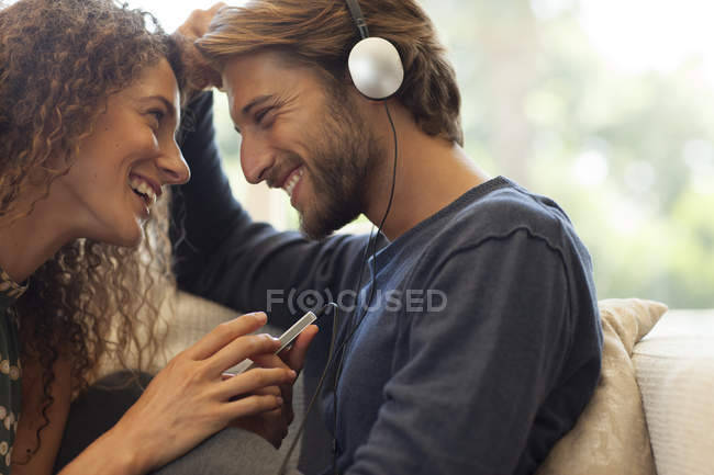 Jovem atraente Casal ouvindo fones de ouvido no sofá — Fotografia de Stock