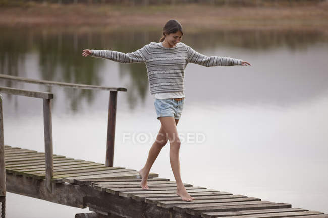 Жінка, що йде на причалі над озером з витягнутими руками — стокове фото