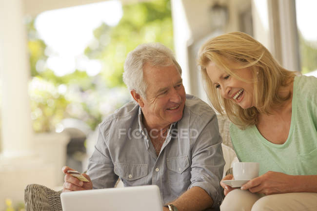 Sonriente pareja bebiendo café y compras en línea en el patio - foto de stock