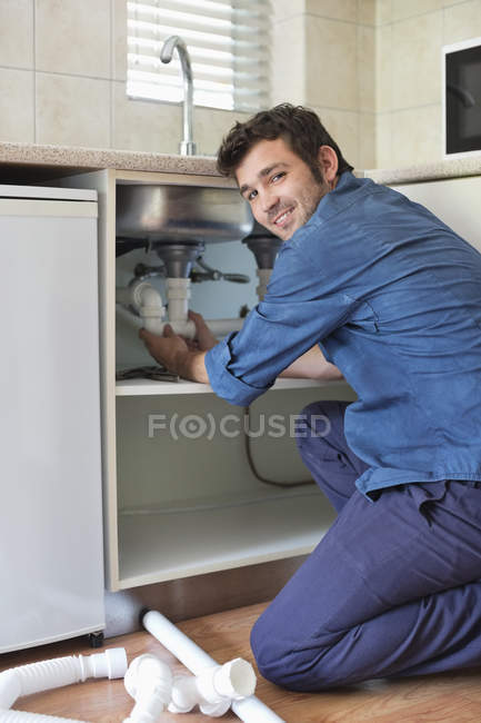Fontanero trabajando en tuberías bajo fregadero de cocina - foto de stock