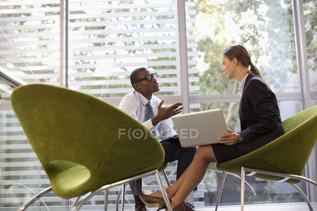 Homme d'affaires et femme d'affaires avec ordinateur portable parlant dans le hall au bureau moderne — Photo de stock