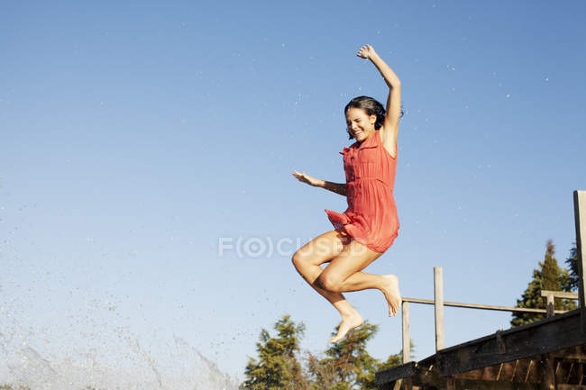 Smiling caucasian woman jumping off dock — Stock Photo