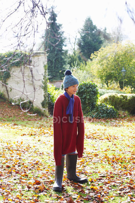Niño vistiendo suéter de padre y botas en el patio trasero - foto de stock