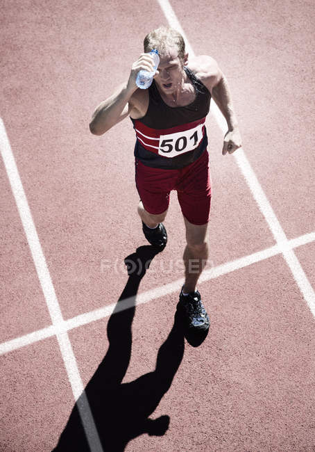 Runner pouring water overhead on track — Stock Photo