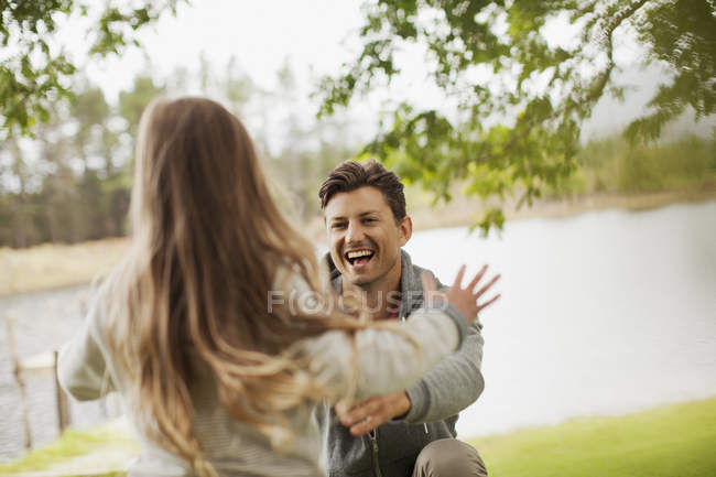 Дочка біжить до усміхненого батька зі зброєю, витягнутою на березі озера — стокове фото