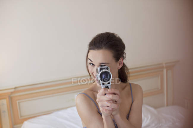 Portrait de femme tenant une caméra vidéo à l'ancienne au lit — Photo de stock