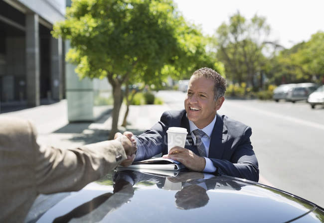 Businessmen shaking hands over car — Stock Photo
