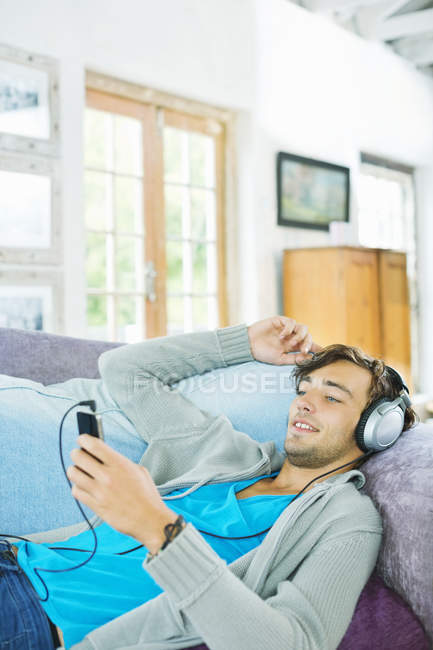 Молодий чоловік слухає навушники на дивані — стокове фото